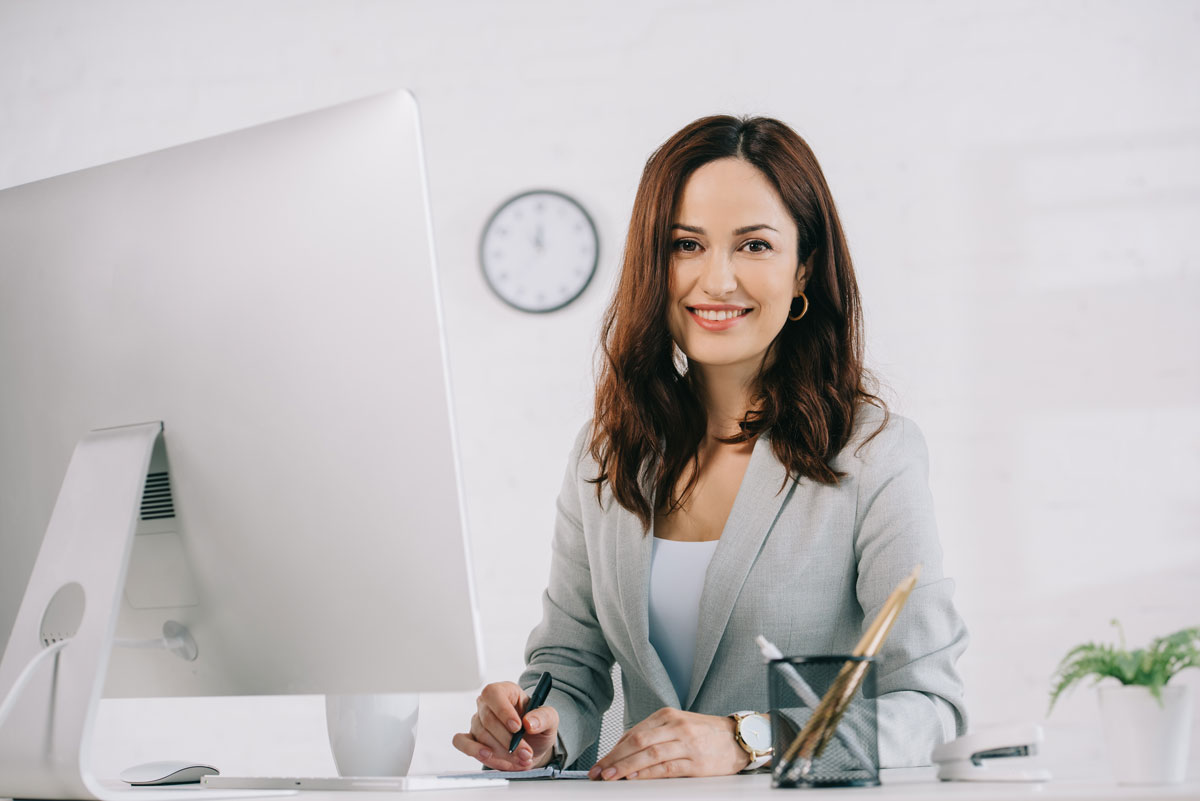 Mitarbeiterin am Computer bei der Arbeit, lächelt in die Kamera